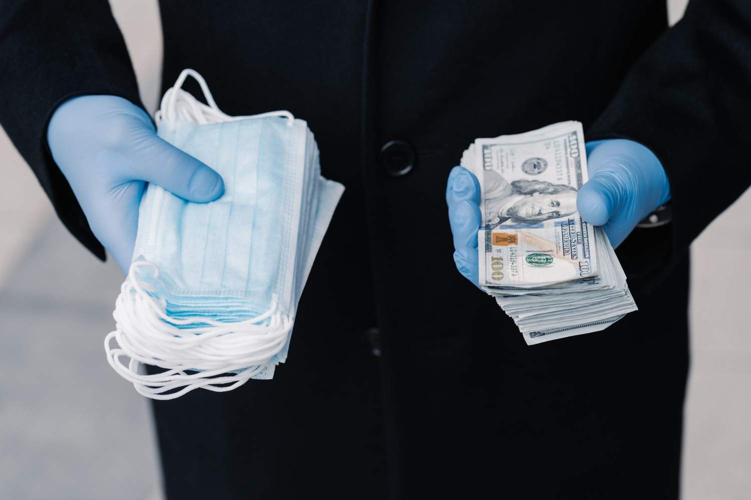 Person in protective medical gloves holds stack of masks and much money